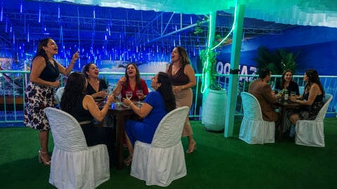 Women socializing at an indoor event venue with blue lighting, green turf floor, and neon green accents