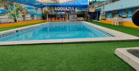 Piscina techada AQUAZUL con agua azul brillante, grass artificial y señalización
