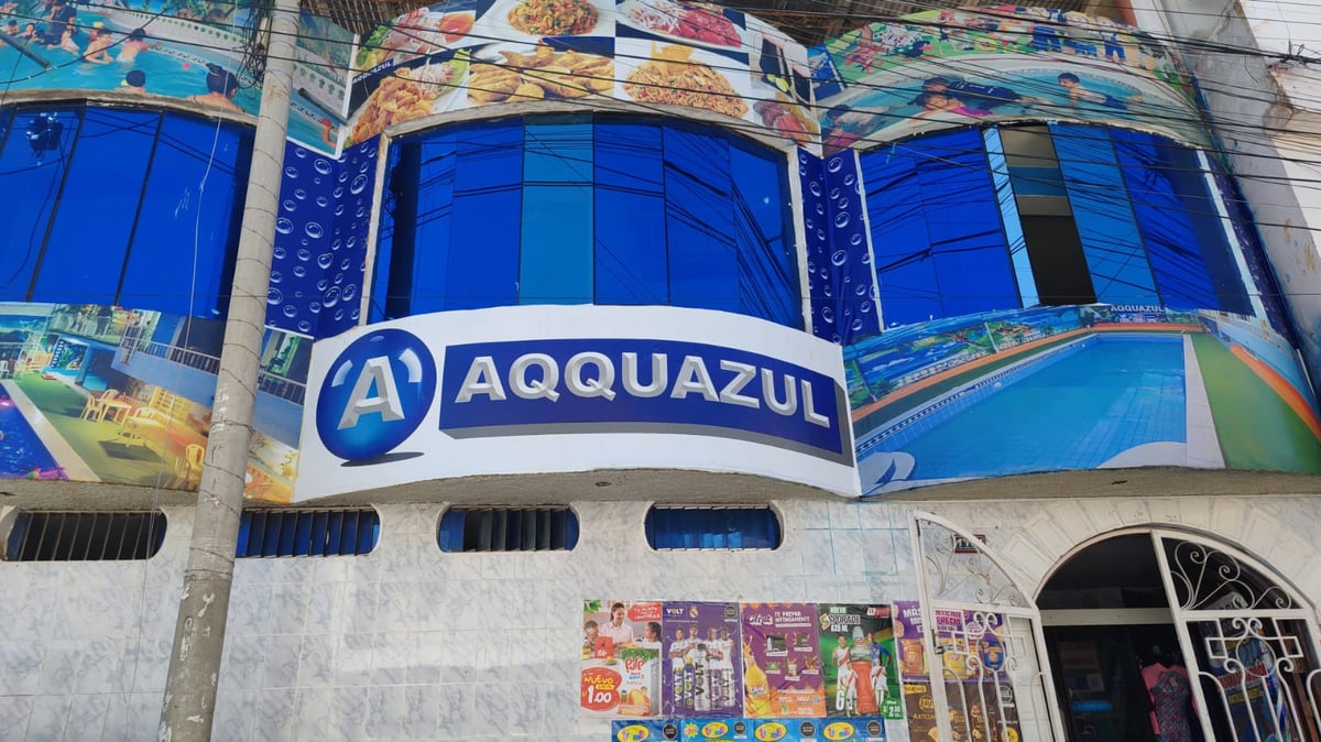 Exterior del edificio AQQUAZUL con ventanas azules curvas y señalización, fachada blanca inferior con entrada, decorado con imágenes acuáticas coloridas