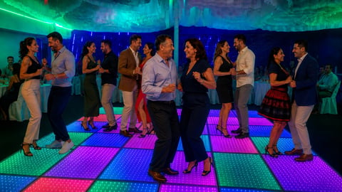 People dancing on a colorful illuminated dance floor at a nightclub with LED lighting and neon ambiance.